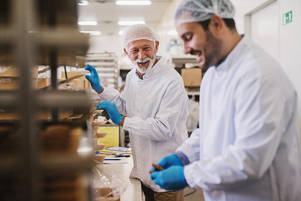 Two people wearing hairnets and gloves are working in a bakery
